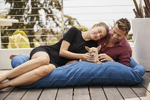 Couple relaxing on a deck with their dog on a blue cushion.